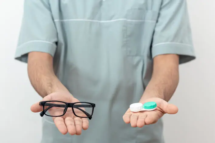 Persona con unas gafas y unas lentillas en cada mano